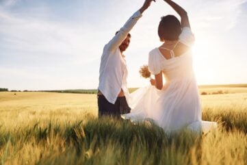 A couple dancing in grass against the sun