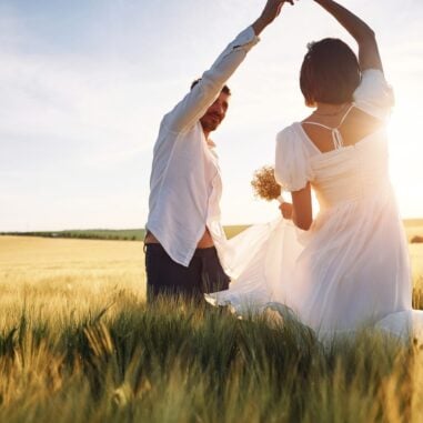 A couple dancing in grass against the sun